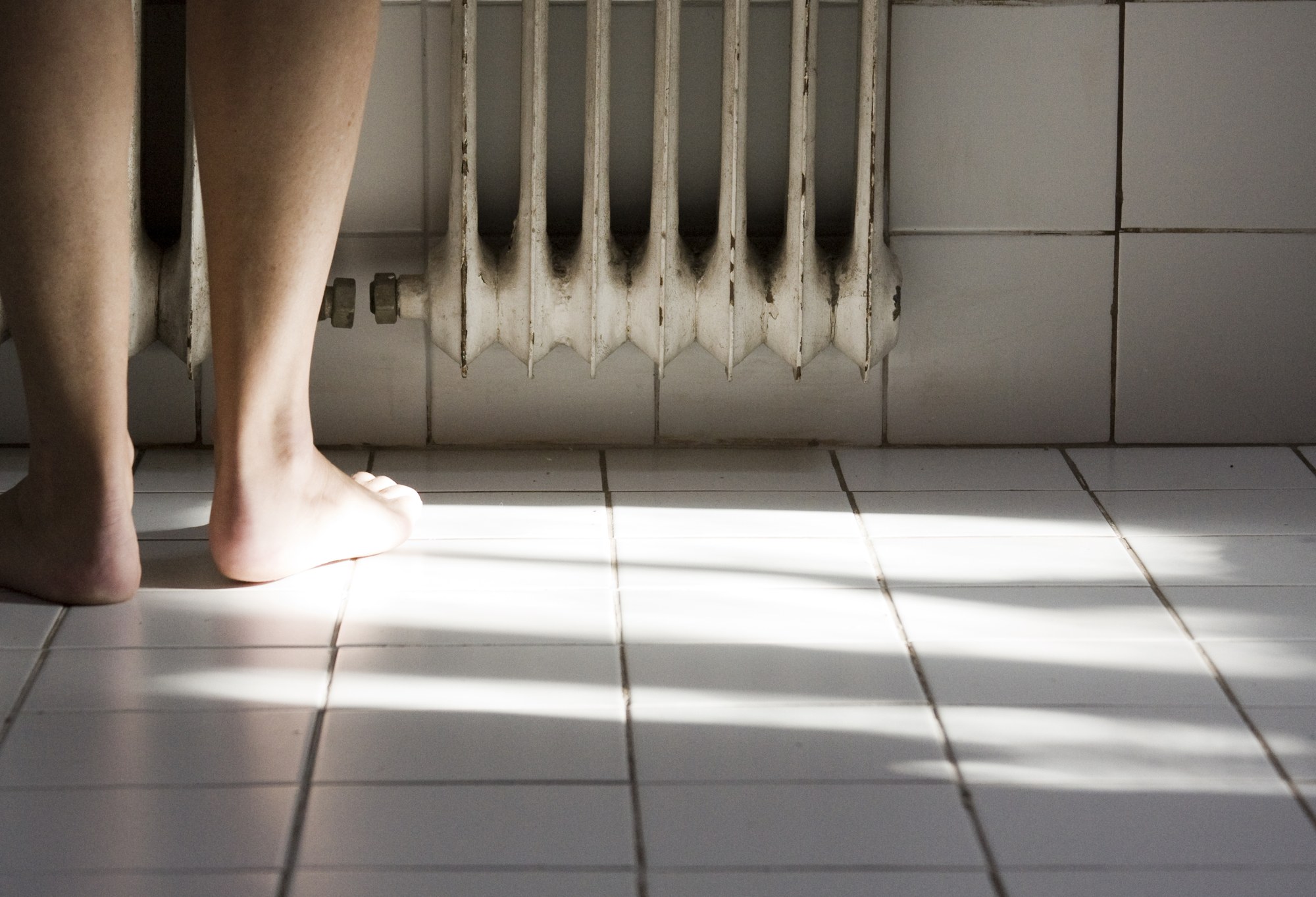 Piernas de una persona junto a un radiador, iluminadas por el sol